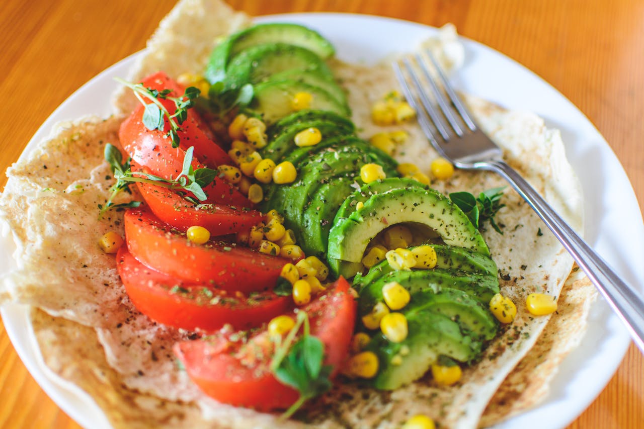 services-04 A vibrant salad with avocado, tomato, and corn on flatbread, topped with herbs, perfect for a healthy meal.
